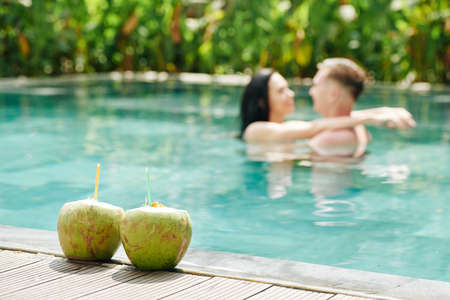 Young couple in love kissing in swimming pool, two refreshing coconut cocktails on foregroundの写真素材