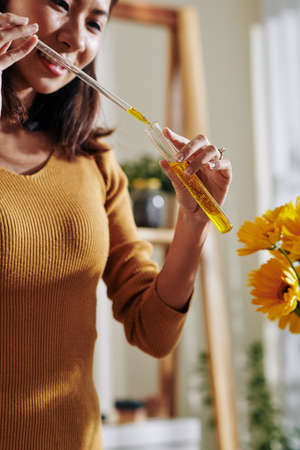 Smiling young Vietnamese woman taking some yellow diluted colorant from test-tube with glass pipetteの写真素材