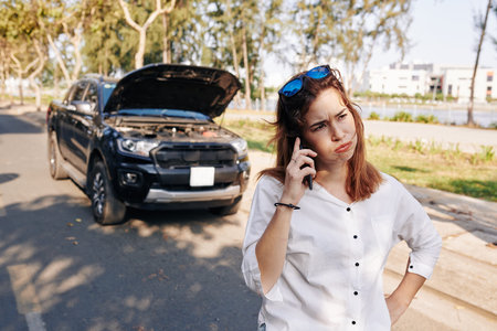 Stressed unhappy young woman calling on phone and discussing car breakdown trouble problem with...
