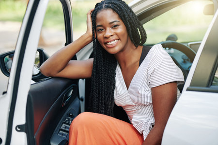 Portrait of cheerful young Black woman with dreadlocks sitting in her new car with opened doorの写真素材
