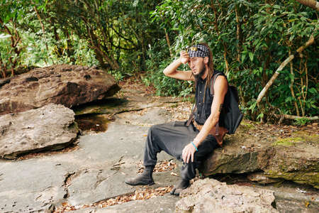 Tired mature man wiping sweat from his forehead after hiking in forestの写真素材