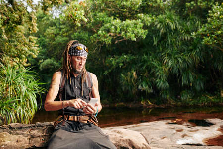 Frowning tousit checking map on his smartphone when he got lost in the forestの写真素材