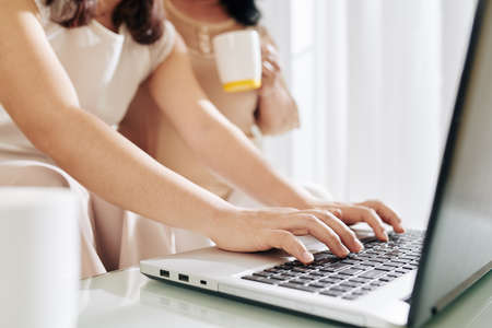 Hands of young woman typing on laptop when helping her senior mother to fill documents for bankの写真素材