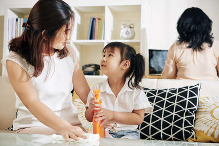Mother teaching her little daughter how to wipe table surface with desinfectant sprayの写真素材