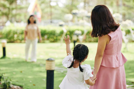 Little girl holding hand of her mother and waving with hand to grandmother in backgroundの写真素材