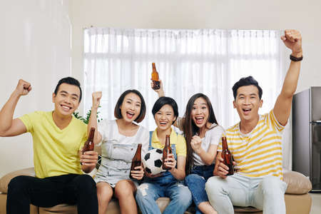 Group of excited football fans drinking beer when watching match online at homeの写真素材
