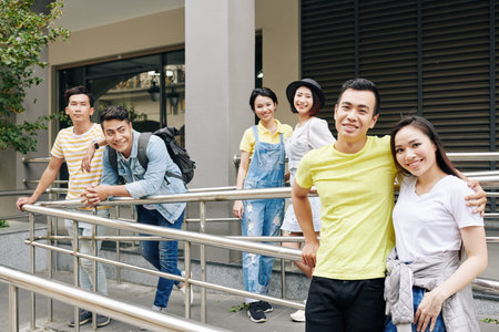 Cheerful Asian students standing on porch of college building