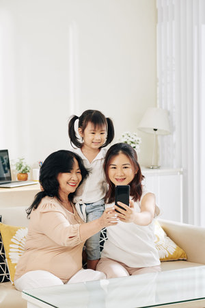 Cheerful little Asian girl, her mother and grandmother taking selfie together