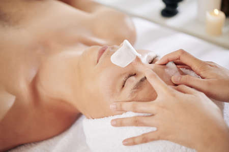 Young man with blackhead remover sticker on his nose enjoying rejuvenating face massage in beauty salonの写真素材