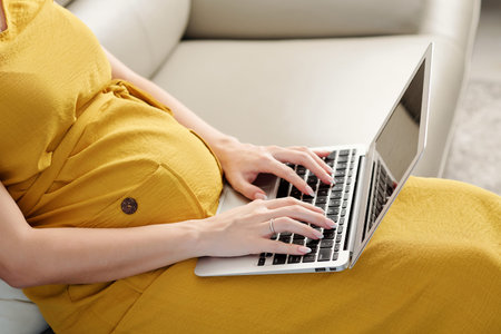 Cropped image of pregnant woman with laptop answering e-mails when working from home during...