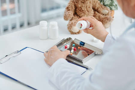 Doctor emptying tablets and pills into metal tray and writing down prescription for patientの写真素材