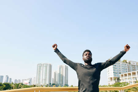 Serious young Black sportsman raising arms when doing exercise for chest openingの写真素材