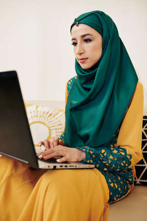 Young beautiful muslim busineswoman staying at home during pandemic and working on laptopの写真素材