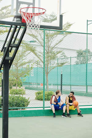Friends sitting out outdoors court, drinking water and talking after playing game of basketballの写真素材