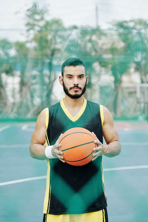 Young handsome serious Hispanic basketball player posing on street basketball courtの写真素材