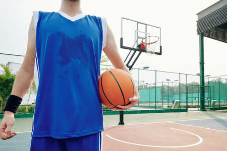 Cropped image of sweaty basketball player standing on outdoor court with ballの写真素材