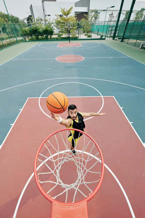 Basketball player jumping and throwing ball in basket, view from above