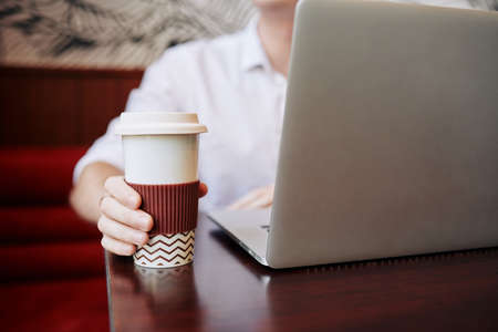 Man drinking coffee from tall tumbler cup when working on laptop in cafeの写真素材