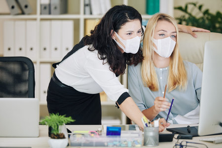 Female boss supervisor in medical mask explaining intern or new employee online task
