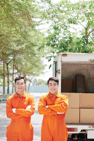 Two happy Vietnamese loaders in bright orange overalls standing in front of truck