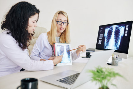 Professional young female pulmonologists pointing at lungs x-ray image on screen of tablet computer...