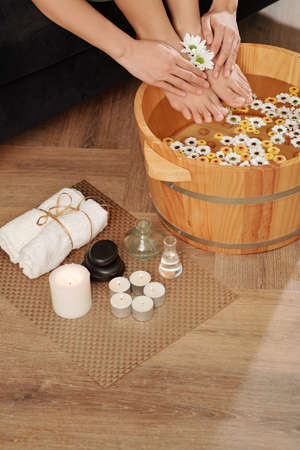 Woman soaking feet in wooden basin with water and daisy flowersの写真素材