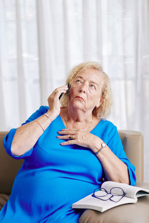 Nervous aged woman touching chest and looking up when talking on phone with family member