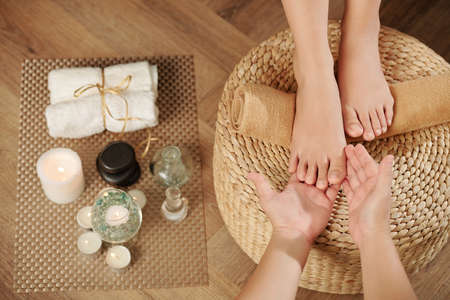 Pedicurist asking female client to put feet on wicker stool so she could examine it before starting procedureの写真素材