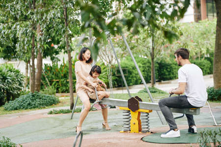 Young mother, father and daughter playing on seesaw in parkの写真素材