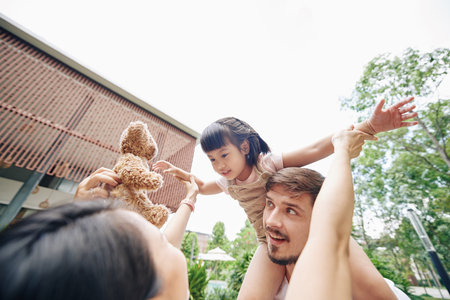 Father carrying daughter over his head and mother giving her teddybearの写真素材