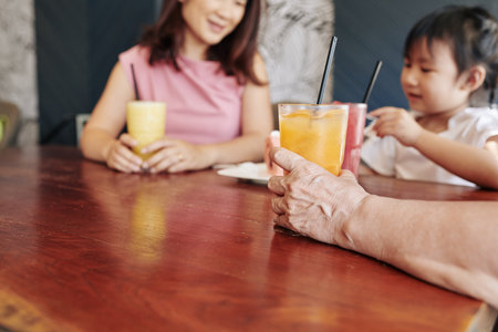 Hand of senior woman drinking fruit cocktail when celebrating birthday of her little granddaughter...