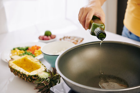 Woman pouring vegetable oil in frying pan to fry rice with vegetables and make traditional dishの写真素材