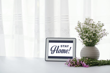 Vase with fresh wild flowers and digital tablet with stay home inscription
