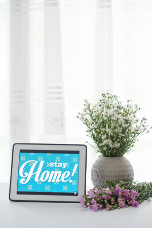 Stay home advice on tablet computer and vase with blooming wild flowers