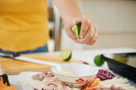 Hand of woman squeezing lime juice in small bowl when making dressing for saladの写真素材