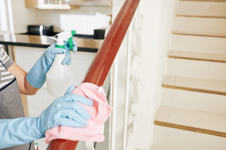 Woman spraying stair railing with cleaning detergent and wiping off dirt and dust