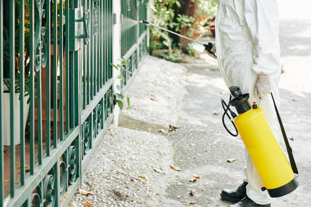 Cropped image of technician spraying fence with chemical to prevent spreding of pneumonia virus in cityの写真素材