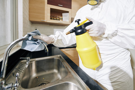 technician in protective overall spraying kitchen tap with detergent and wiping with soft clothes