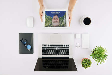 Businesswoman video calling her senior father to discuss news when sitting at table with laptop, coffee and glassesの写真素材