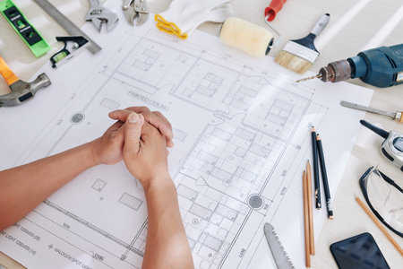 Construction engineer sitting at desk with working tools and blueprint of house