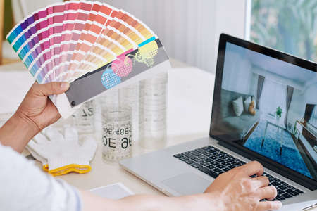 Interior designer looking at inspiring photos on laptop screen and choosing color for walls color from paletteの写真素材