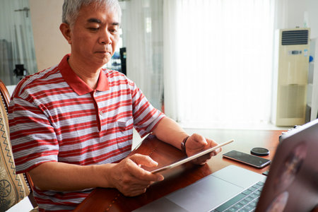 Senior Chinese man looking at photos on tablet computer that he just edited for client
