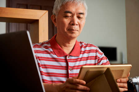 Elderly Chinese man working from home during quarantine, he is putting tablet computer on tablet standの写真素材