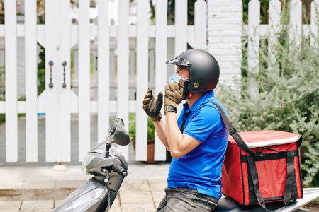 Courier on scooter with cooler bag calling on phone to customer to specify details of contact free deliveryの写真素材