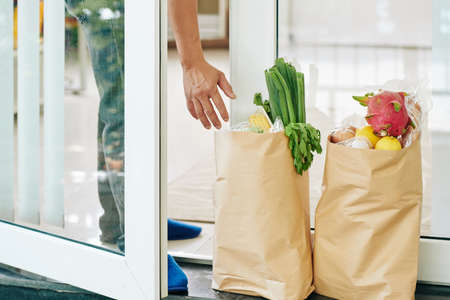 Close-up image of customer taking packages with fresh food that were delivered to doors of his houseの写真素材