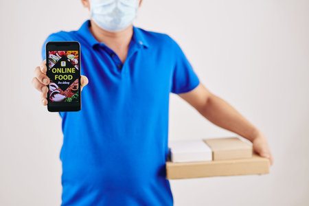 Cropped image of delivery man in medical mask holding pizza boxes and showing smartphoe with opened...