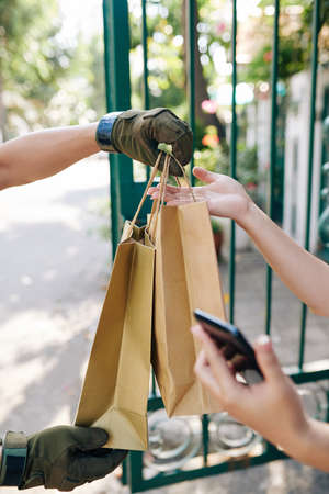 Woman receiving delivery and paying for two packages with banking app on her smartphoneの写真素材