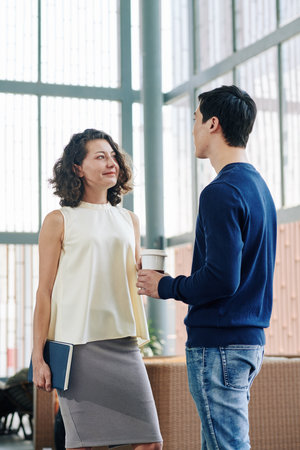 Smiling pretty young businesswoman looking at colleague telling about his project