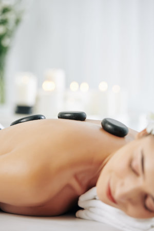 Close-up image of young woman lying on bed in spa salon with hot basalt stones along her spine