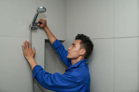 Plumber in uniform using wrench when installing shower head in bathroomの写真素材